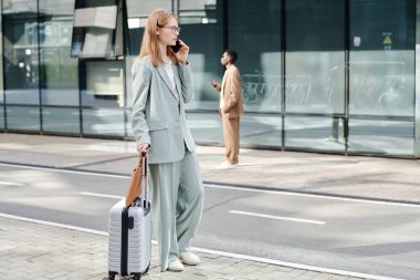 Kafkasyalı genç iş kadını bavuluyla dışarıda dikilirken ve telefonla konuşurken geniş açılı görüntüsü, kopyalama alanı.