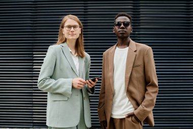 Orta boy etnik çeşitlilikteki Z erkek ve kadın şık kıyafetler giyip iş alanında portre için poz verirken.