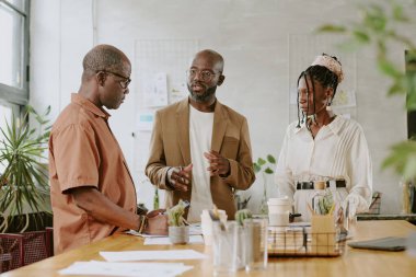 Ciddi Afrikalı Amerikalı patron, astlarıyla modern ışık ofisinde toplantı yapıyor.