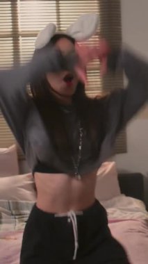 Asyalı kızın k-pop şarkısı ve dudak senkronizasyonu eşliğinde evde trend videolar kaydederken dikey görünümü