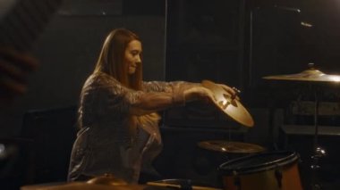 Bilinmeyen erkek gitarist eşliğinde canlı performansa hazırlanırken beyaz kadın müzisyenin zilleri ayarladığı orta boy bir fotoğraf.