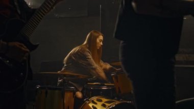 Sahnede canlı performanstan önce tanınmayan erkek müzik grubu arkadaşlarıyla vurmalı perküsyon enstrümanları kuran beyaz kadın davulcunun orta boy çekimi.