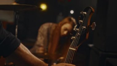 Kimliği belirsiz erkek müzisyenin elektro gitar alıp davul ve şapka ayarlayan kadın grup arkadaşlarıyla canlı performansa hazırlandığı yakın plan.