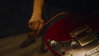 Elektro gitar takan, ses kontrolü yapan ve konser salonundaki canlı performansa hazırlanan tanınmayan erkek müzisyenlerin elleri yakın plan çekimde.