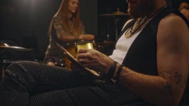 Genç beyaz müzisyenin portresi, kayıt stüdyosunda grup arkadaşlarıyla birlikte canlı performanstan önce oturup, perküsyon enstrümanları kurarak ve pratik yaparak deftere yazı yazması.