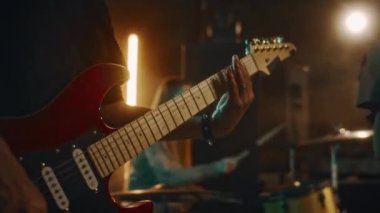 Kafkasyalı genç müzisyenin müzik seansı sırasında ya da grup arkadaşlarıyla yaşam performansı sırasında loş ışık stüdyosunda elektro gitar çalmasının yakın çekimi.