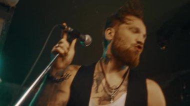 Sahnede elinde mikrofonla şarkı söyleyen, zevk ve tutkuyla şarkı söyleyen beyaz erkek vokalistin orta boy yakın çekimi.