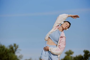 Spor giyimli yaşlı bir kadının parkta boş zaman geçirirken yan eğik durduğu düşük açılı bir çekim.