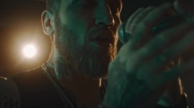 Canlı müzik konseri sırasında sahnede şarkı söylerken duygusal olarak mikrofona bağıran genç beyaz erkek vokalistin yüzünü ve ellerini kapatın.