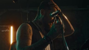 Sahnede mikrofon tutan ve konser sırasında elektro gitar ve perküsyon çalan grup arkadaşlarıyla şarkı söyleyen orta boy beyaz erkek vokalist.