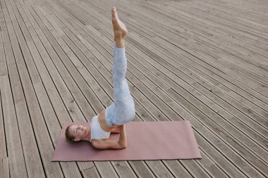 High angle shot of young blonde woman in top bra and leggings standing in shoulder stand on deep pink mat clipart