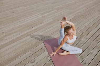 High angle shot of young woman sitting on deep pink rose mat and stretching her leg muscle clipart