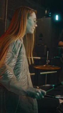 Sahnede orta yaşlı erkek gitaristle çalarken, profesyonel beyaz kadın davulcunun perküsyon enstrümanları çalarken orta boy dikey çekimi.