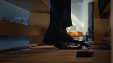 Siyah ayakkabılı, ayakları pedaldan bençe hareket ettiren tanınmamış org çalgıcısının bacaklarının yakın plan çekimi.