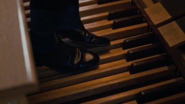Siyah pantolon ve ayakkabıyla kilisenin orgu üzerinde ustalıkla pedal çeviren tanınmamış ustanın ayaklarına yakından bakın.