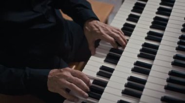 Siyah elbiseli, org klavyesi çalan, kimliği belirsiz bir erkek oyuncunun yakın plan çekimleri.