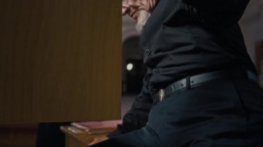 Orgun ahşap bankında oturan yaşlı orgcuyu yukarı kaldır, esmer kadın arka planda gülümsüyor.