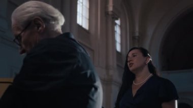 Esmer kadın şarkıcı ve gri saçlı erkek orgcunun katedralde birlikte performans sergilediği düşük açılı çekim.