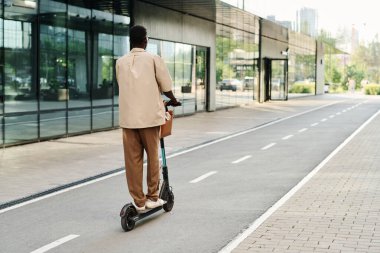 Tanımlanamayan siyah adamın arka görüntüsü şık günlük kıyafetler giyen iş alanı caddesi boyunca elektrikli scooter süren siyah adam.