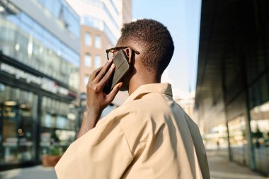 İş bölgesinde dışarıda dikilirken telefonla konuşan tanınmayan Afro-Amerikalı genç adam.
