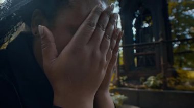 Mezarlıkta ağlarken yüzünü elleriyle kapatan siyah giysili yas tutan kadının yakın görüntüsü.