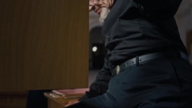 Orgun ahşap bankında oturan yaşlı orgcuyu yukarı kaldır, esmer kadın arka planda gülümsüyor.
