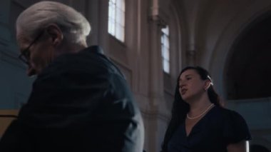 Esmer kadın şarkıcı ve gri saçlı erkek orgcunun katedralde birlikte performans sergilediği düşük açılı çekim.
