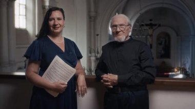 Koyu mavi elbiseli esmer kadın şarkıcının portresi. Müzik notaları ve siyah gömlekli yaşlı erkek orgcu ve kilise balkonunda kameraya poz veriyor.