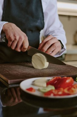 Ortanca, tanınmayan erkek şefin elleri ahşap kesim tahtasıyla mozzarella dilimliyor.