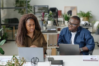 Diz çöküp, güzel kıvırcık saçlı bayan meslektaşına ofisinde yardım eden Afro-Amerikalı bir adam.