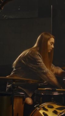 Uzun saçlı genç bayan davulcunun müzik grubuyla konser vermeden önce sahnede davul seti hazırlarken dikey çekimi.