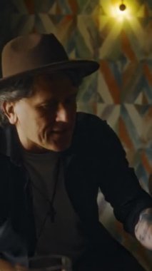 Orta yaşlı müzisyenlerin kağıt ve kalem tutarken barda grup arkadaşlarıyla yeni şarkı fikirlerini tartışırken çekilmiş dikey bir fotoğrafı.