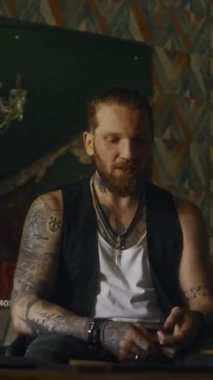 Sakallı, kadın grup arkadaşıyla barda takılırken gülümseyen ve sohbet eden dövmeli müzisyenin dikey çekimi.