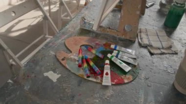 Sanat stüdyosunun masasındaki ahşap palette beş guaj boya tüpü ve dört balmumu boya kalemi çeken yok.