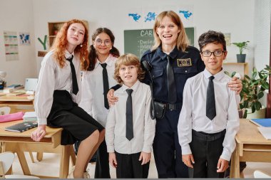 Kariyer gününde sınıfta resim çektirmek için poz veren neşeli bayan polis memuru ve bir grup genç kız.