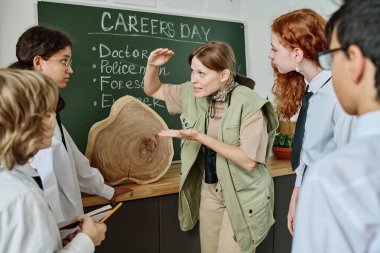 Joyful female forester standing in classroom telling about dendrochronology during career guidance class at school clipart