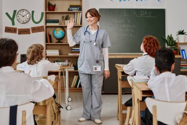 Okuldaki kariyer gününde üniformalı bir grup genç öğrenciyi karşılayan bir kadın doktor.