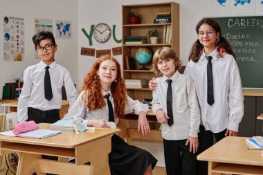 Sınıfta kameraya poz veren dört farklı genç kız ve erkek çocuk grubu, orta boy portre.