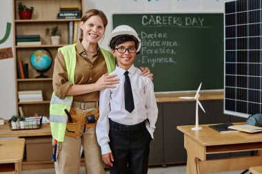 Neşeli beyaz kadın mühendis ve çift ırklı genç öğrenci okuldaki kariyer gününde sınıfta kameraya poz veriyorlar.