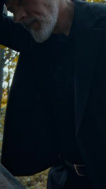 Üzüntülü orta yaşlı bir adamın dikey yatay çekimi, kayıpla baş etmek, mezarlıkta mezar taşına yaslanmak.