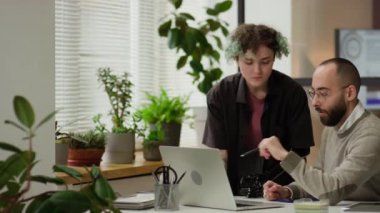 Genç bayan ofis çalışanı ve erkek yönetici dizüstü bilgisayarı işaret ederek projeyi tartışıyorlar