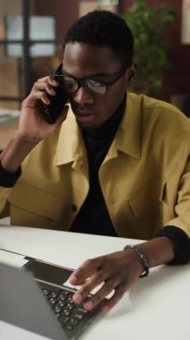 Afrikalı Amerikalı genç girişimcinin iş yerindeki müşteriyle telefonda konuşurken dikey çekimi.