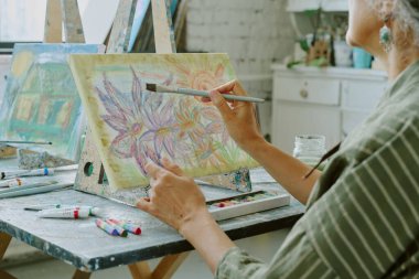 Sanat terapisi sırasında beyaz tuvale renkli büyük çiçek tomurcukları çizen tanınmayan yaşlı bir kadının orta derecede yakın çekimi.