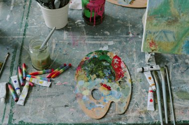 Eski masanın üstünde akrilik boya, fırça ve tuvalle kirli ahşap paletin en üstteki görüntüsü.