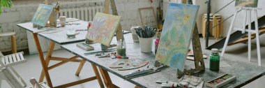 Website banner with three paintings on canvas, different types of paints and brushes on wooden table clipart