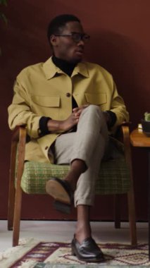 Afrikalı Amerikalı bir gencin bacak bacak bacak üstüne atmış bir şekilde koltukta otururken iş arkadaşıyla konuştuğu dikey çekim.