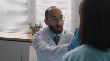 Beyaz önlüklü ve eldivenli erkek estetik cerrahın kadın hastanın yüzünü incelemesi ve klinikte ameliyat öncesi konsültasyon yapması sayesinde.