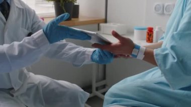 Hastane önlüklü genç bir bayanı yatakta otururken, doktordan dijital tablet alırken ve estetik ameliyattan önce bu konuda tıbbi anlaşma imzalarken çek.