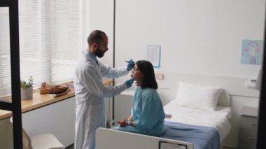 Beyaz önlüklü ve eldivenli profesyonel doktor hastane koğuşunda estetik ameliyata hazırlanırken genç bayan hastaların yüz bölgelerini işaretliyor.