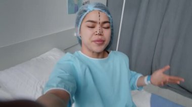 Yüzünde ameliyat öncesi işaretler olan Z jenerasyonu kızı hastane yatağında uzanıyor, sosyal medyada canlı yayında el sallıyor ve konuşuyor.